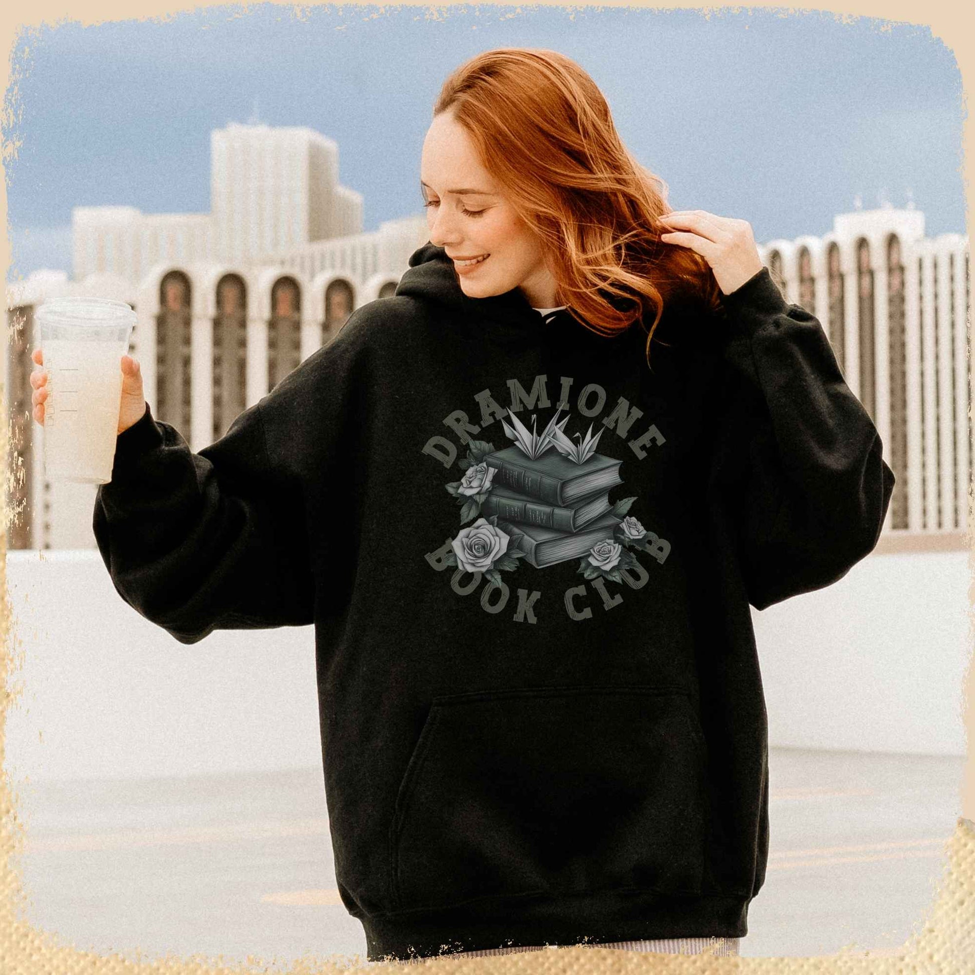 Eine junge Frau trägt einen Hoodie mit einem grünen Dramione Book Club Motiv, mit einer Schrift im Collegelook.