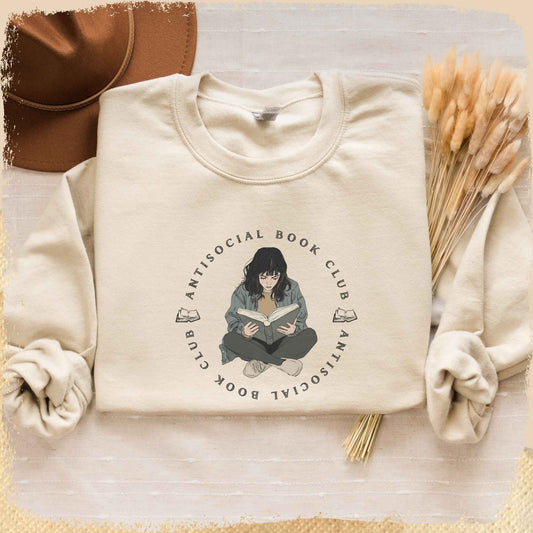 Ein sandfarbenes Book Sweatshirt mit einem gezeichneten introvertierten Büchermädchen, das von einem Schriftzug "Antisocial Book Club" umgeben ist.
