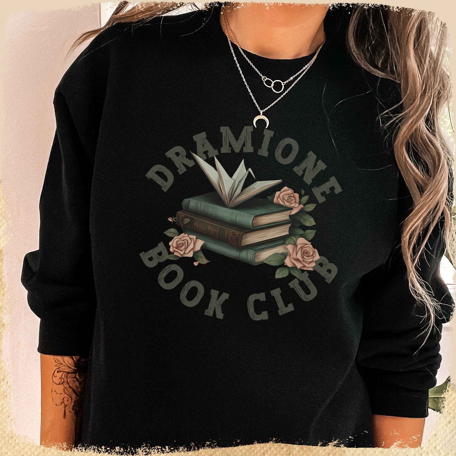 Man sieht ein Book Sweatshirt mit dem Schritzug "Dramione Book Club" im Collegelook. In Der Mitte ist ein Bücherstapel,auf dem ein Papierkranich sitzt. Der Stapel wird von Rosen umspielt.