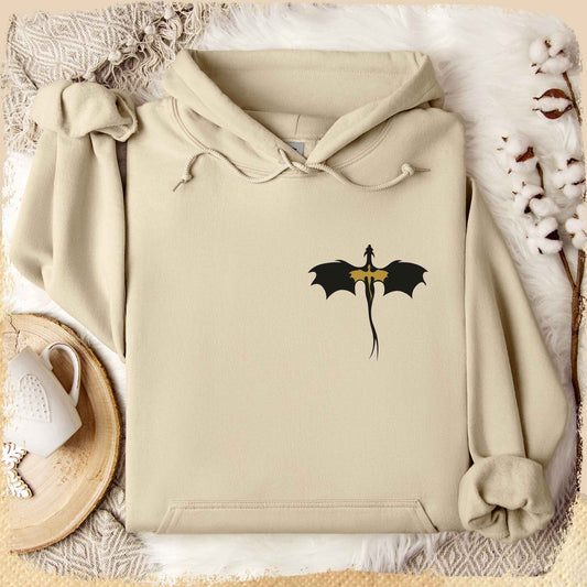 Ein sandfarbener Hoodie mit einem Drachenmotiv. Die Silhouette eines kleinen goldenen Drachen auf der Silhouette eines größeren schwarzen Drachen.